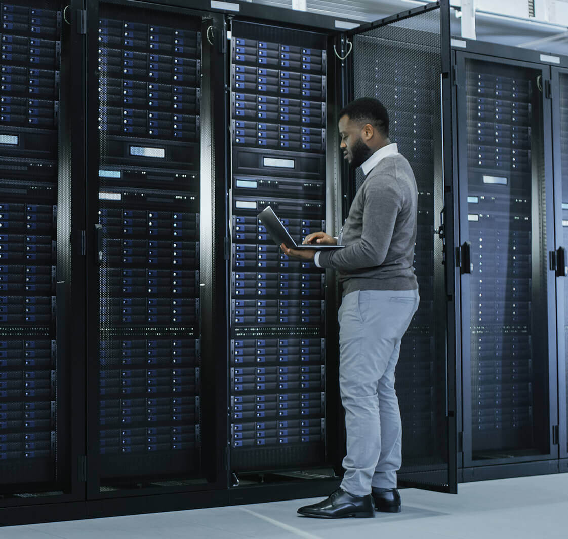 IT Specialist is Working on Laptop in Data Centre while Standing Before Server Rack.