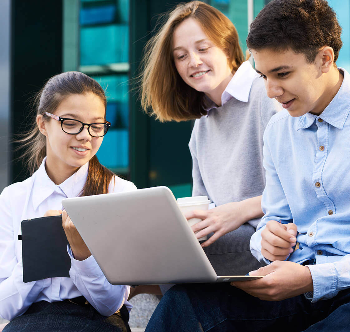 Three school children using a laptop and tablet outside.