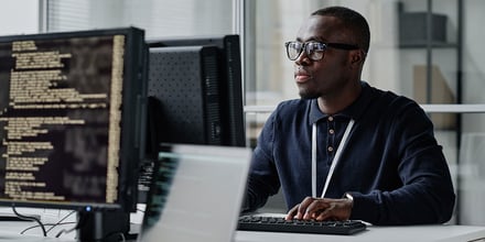 Young developer in eyeglasses concentrating on his online work on computer sitting at workplace.