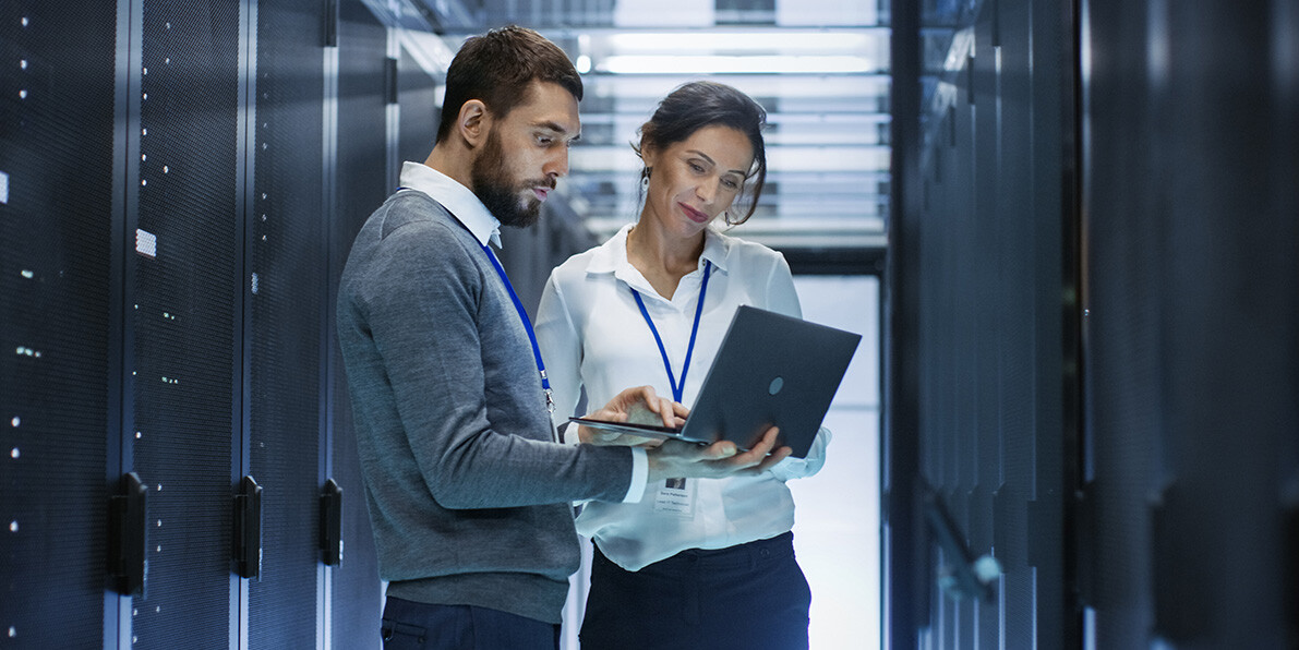 Male IT Specialist Holds Laptop and Discusses Work with Female Server Technician.