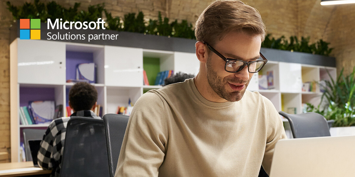 Young focused man wearing eyeglasses working on laptop while sitting at desk in a modern coworking space